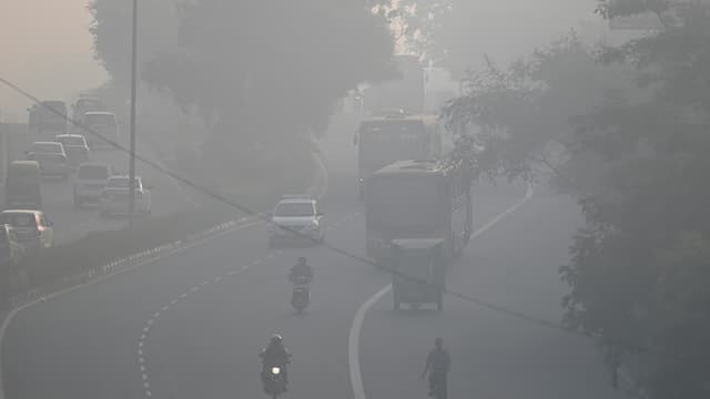 Des habitants de banlieues roulent le long d'une route dans un contexte de smog intense à New Delhi, le 21 novembre 2021.