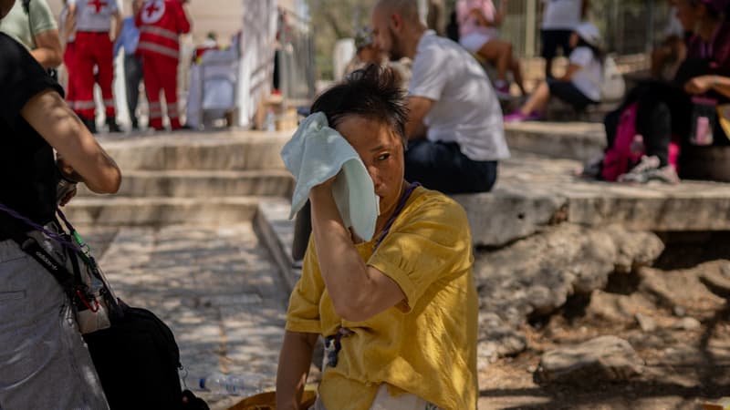 Une touriste s'essuie le visage avec une serviette devant le site monumental fermé de l'Acropole à Athènes, le 23 juillet 2025.