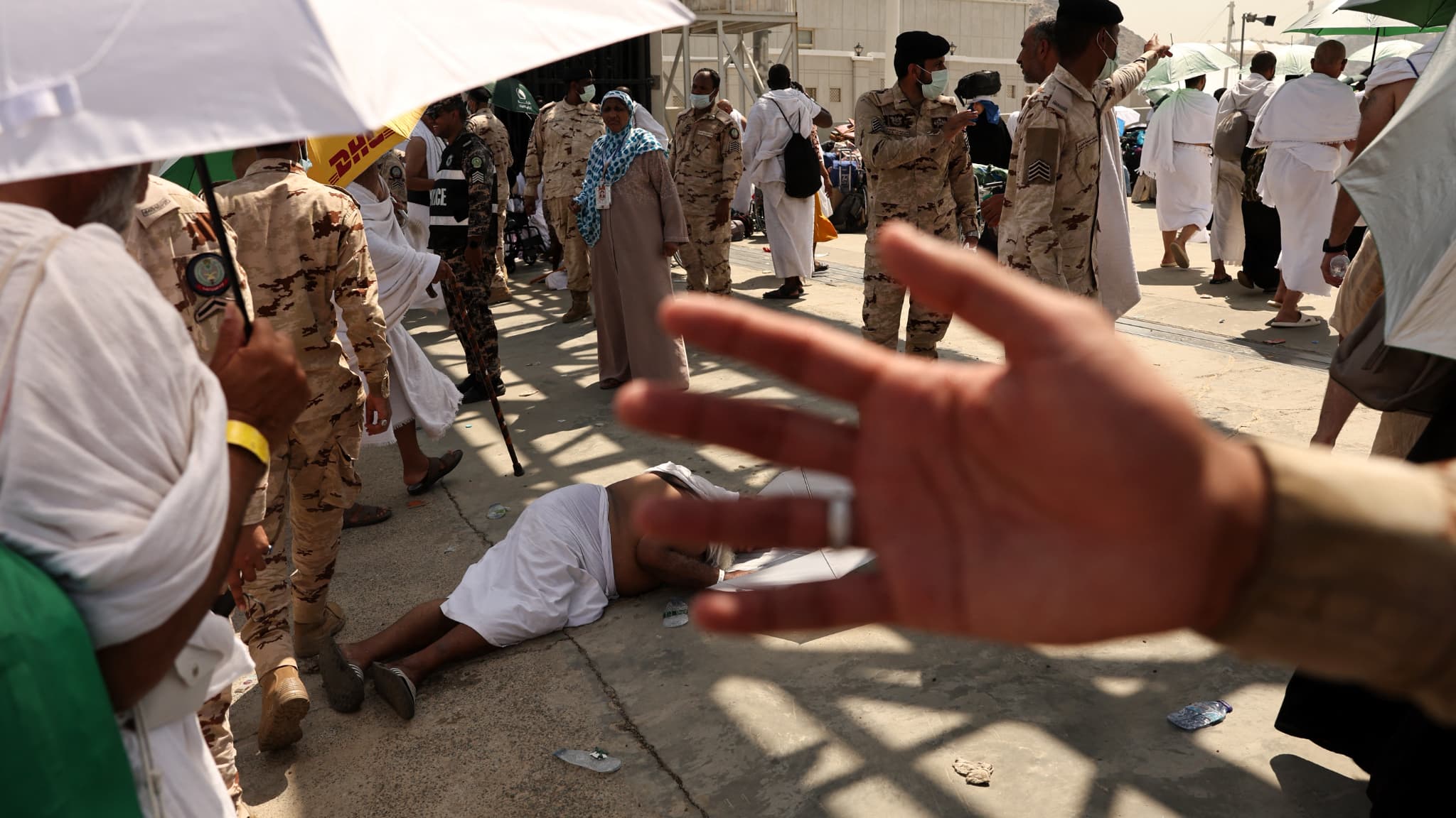 Un membre des forces de sécurité saoudiennes empêche les gens de s'approcher alors qu'un homme souffrant de la chaleur torride est allongé sur le sol lors du hajj à Mina, le 16 juin 2024. Un membre des forces de sécurité saoudiennes empêche les gens de s'approcher alors qu'un homme souffrant de la chaleur torride est allongé sur le sol lors du hajj à Mina, le 16 juin 2024.