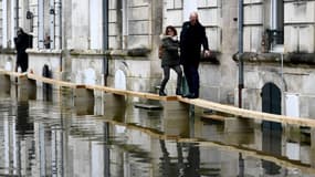 Des piétons circulent sur des ponts de fortune dans une rue inondée de Saintes, en Charente-Maritime, le 15 décembre 2023