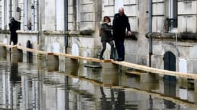 Des piétons circulent sur des ponts de fortune dans une rue inondée de Saintes, en Charente-Maritime, le 15 décembre 2023