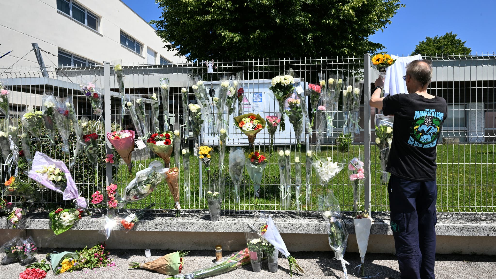 Un homme accroche des fleurs sur la clôture du collège Françoise Dolto à Nogent (Haute-Marne), le 11 juin 2025, au lendemain de l'arrestation d'un lycéen après le meurtre d'une assistante d'éducation lors d'une fouille de sac