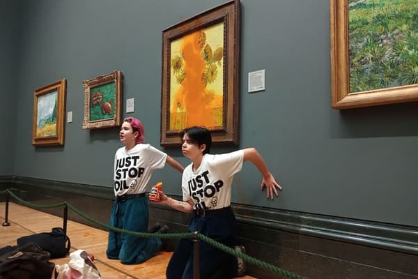 Des activistes de "Just Stop Oil" les mains collées au mur sous les "Tournesols" de Vincent van Gogh après avoir jeté de la soupe à la tomate sur le tableau à la National Gallery, dans le centre de Londres, le 14 octobre 2022.