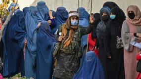 Un combattant taliban monte la garde devant des femmes qui attendent pour une distribution d'argent organisée par le Programme alimentaire mondial, à Kaboul le 29 novembre 2021
