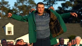 Le numéro un mondial, l'Américain Scottie Scheffler, vainqueur du Masters, enfile la traditionnelle veste verte, remise par le précédent vainqueur, le Japonais Hideki Matsuyama, le 10 avril 2022 à Augusta (Géorgie