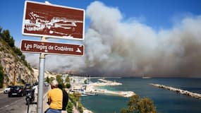 La plage des Corbières, à Marseille, dans le sud de la France, le 8 juillet 2025, des passants observent la fumée d'un incendie de forêt qui fait rage en arrière-plan