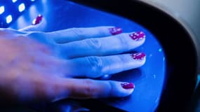 Une main manucurée dont le vernis est en train de sécher sous une lampe à UV.