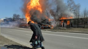 Un habitant passe à proximité d'un véhicule et d'un bâtiment en feu après un tir d'artillerie russe, le 25 mars 2022 à Kharkiv