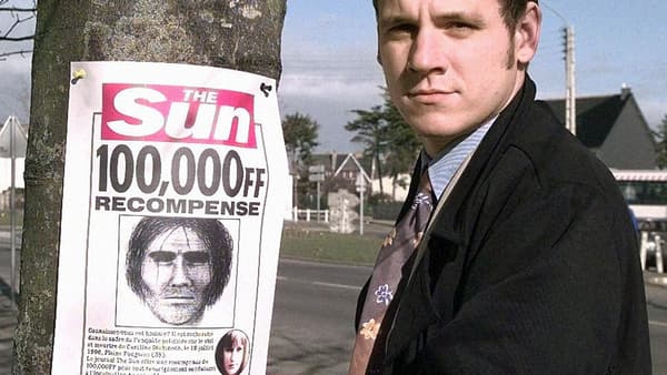 Un journaliste britannique pose à côté d'un avis de recherche du suspect dans l'affaire Dickinson. Un journaliste britannique pose à côté d'un avis de recherche du suspect dans l'affaire Dickinson.