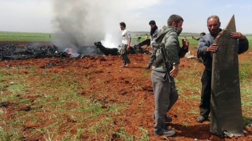 Des syriens armés vérifient les débris d'un avion abattu, une attaque revendiquée par un groupe rebelle allié à Al-Qaïda au dessus de la localité d'al-Eis le 5 avril 2016, dans le nord de la Syrie, une opération auparavant attribué aux j...