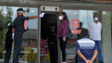Un agent de sécurité prend la température d'une femme avant qu'elle entre dans un centre commercial, le 8 juin 2020 à Siliguri, en Inde