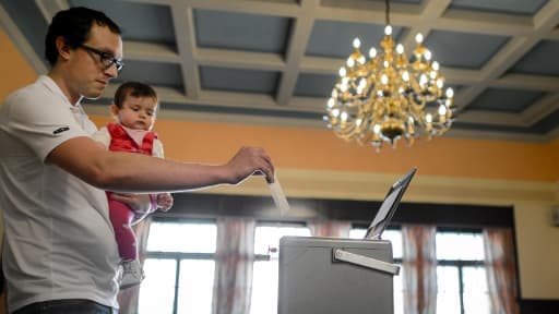 Un père vote dimanche à Bulle, en Suisse, à l'occasion du référendum sur l'instauration d'un salaire minimum/