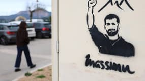 Une femme passe devant un graffiti mural représentant Massimu Susini, un homme menacé pour sa position publique contre le trafic de drogue et tué en 2019, lors de la première conférence anti-mafia du collectif Massimu Susini à Cargèse, sur l'île méditerranéenne française de Corse, le 1er mars 2025.