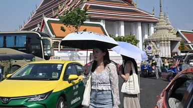 Des touristes se protègent du soleil avec des parapluies pour lutter contre la chaleur à l'extérieur du temple bouddhiste Wat Pho à Bangkok, le 1er avril 2024. 