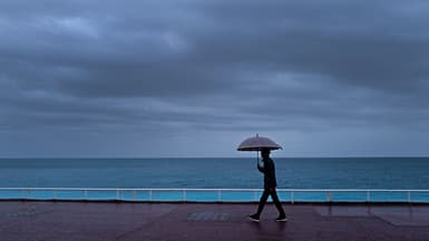 Un passant s'abrite de la pluie sous un parapluie, le long de la plage sur la "Promenade des Anglais" à Nice, le 30 octobre 2023. Photo d'illustration