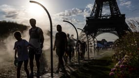 Des personnes se rafraîchissent avec des jets d'eau à côté de la Tour Eiffel à Paris le 29 juillet 2024, pendant les Jeux Olympiques de Paris 2024.