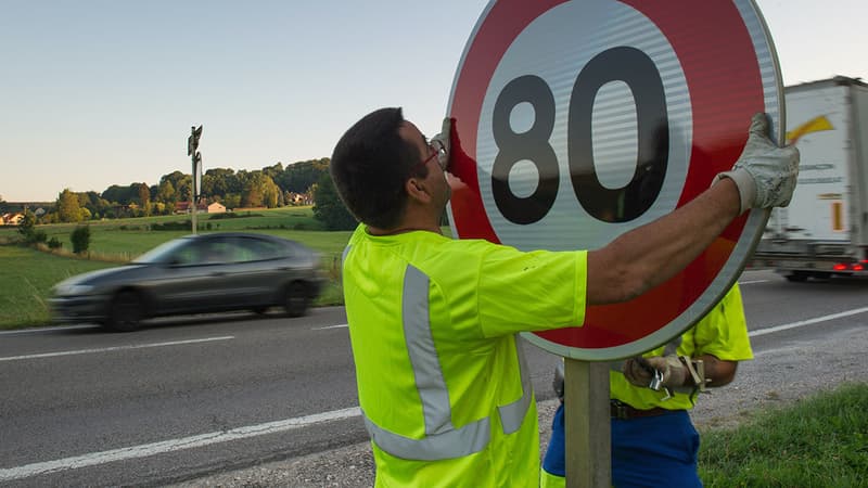 Un employé retirant un panneau de limitation à 80 km/h 