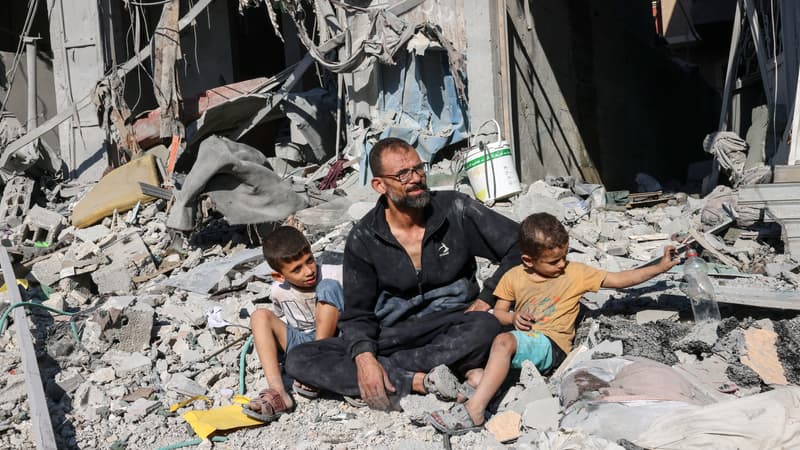 Un Palestinien est assis ses deux enfants devant un bâtiment détruit par une frappe aérienne israélienne à Rafah, dans le sud de la bande de Gaza, le 12 octobre 2023.