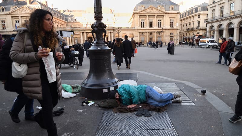 Un SDF endormi dans les rues de Paris et quelques passants pressés, en décembre 2017.
