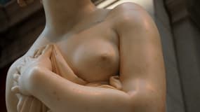 Une statue de femme se couvrant partiellement la poitrine. 