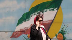 Une femme iranienne passe devant un drapeau iranien peint sur un mur dans une rue de Téhéran, le 10 avril 2023.