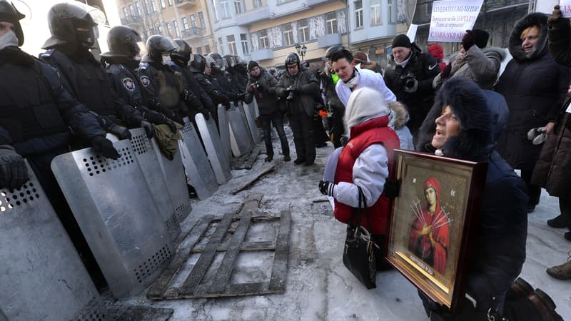 Des manifestants portant des icônes sont agenouillés face aux policiers anti-émeutes, le 24 janvier, à Kiev.