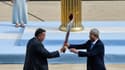 Le vice-président du Comité olympique chinois Yu Zaiqing (à droite) reçoit la torche olympique des mains du patron de l'olympisme grec Spyros Capralos, lors d'une cérémonie à huis clos à Athènes, le 19 octobre 2021