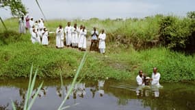 Des membres de la "secte chrétienne apostolique" du Zimbabwe faisant entrer un enfant dans une rivière lors d'une cérémonie religieuse en 1987