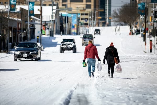 Des personnes marchent au milieu d'une rue enneigée, portant des sacs de provisions, à Austin, au Texas, le 15 février