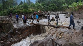 Des habitants traversent la rivière, une journée après l'immense glissement de terrain qui a eu lieu à l'est de l'Ouganda.