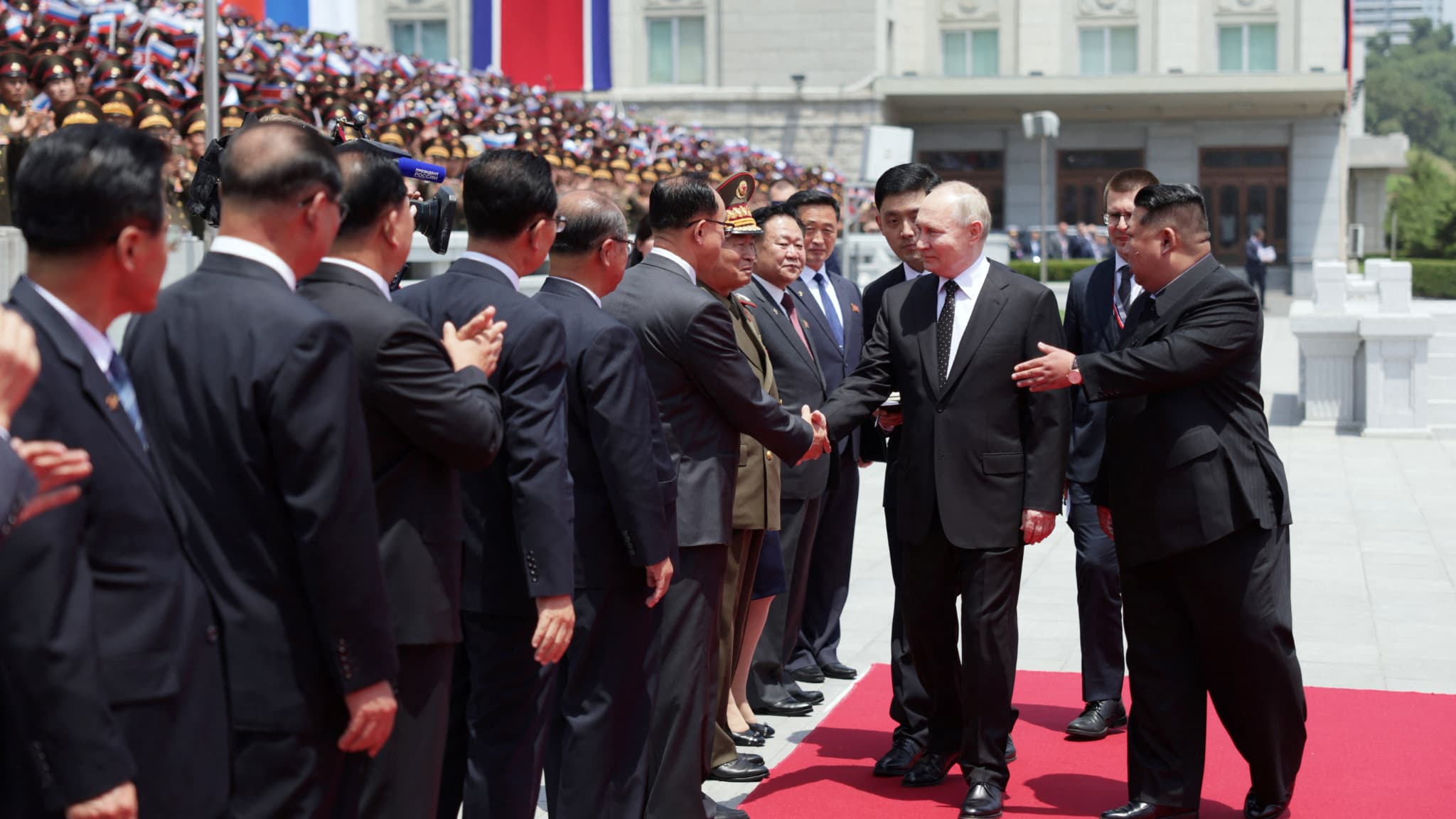 Le dirigeant nord-coréen Kim Jong Un regarde le président russe Vladimir Poutine serrer la main de représentants officiels lors d'une cérémonie de bienvenue sur la place Kim Il Sung à Pyongyang, le 19 juin 2024.