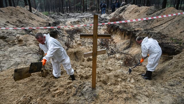 Deux techniciens médico-légaux creusent près d'une croix dans une forêt à la périphérie d'Izyum, dans l'est de l'Ukraine, le 16 septembre 2022. 
