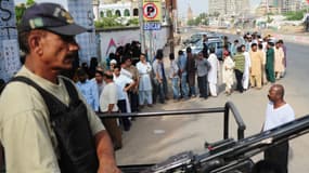 Des habitants de Karachi font la queue devant un bureau de vote, samedi, sous la protection d'un membre des forces de l'ordre.