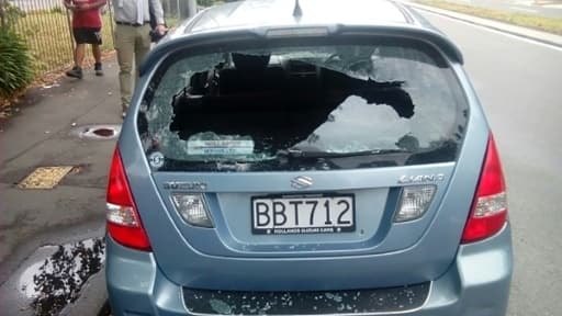 Des passants se tiennent près d'une voiture aux vitres brisées près de la mosquée où s'est produit une fusillade, le 15 mars à Christchurch