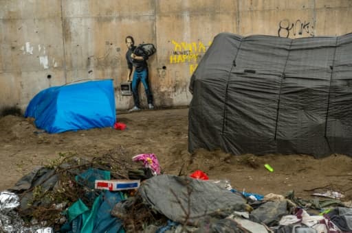 Des tentes de migrants devant une oeuvre de l'artiste britannique Bansky photographiée le 12 décembre 2015 et située à l'entrée de la "Jungle" de Calais, représente Steve Jobs (Apple), qui porte un baluchon et un vieil ordinateur