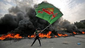 Un manifestant tient un drapeau avec un slogan chiite et le logo du Hezbollah irakien durant une manifestation le 2 octobre à Bagdad