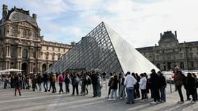 Des visiteurs font la queue devant la Pyramide du Louvre, conçue par l'architecte sino-américain Ieoh Ming Pei, et le musée du Louvre le jour de sa réouverture après un vol de bijoux, le 22 octobre 2025 à Paris
