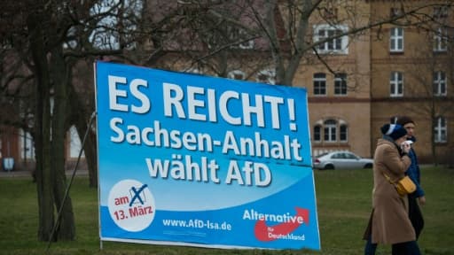 Un couple marche près d'une affiche de campagne du parti Alternative pour l'Allemagne (AfD), portant le slogan "ça suffit !", le 11 mars 2016 à Magdebourg, en Allemagne Un couple marche près d'une affiche de campagne du parti Alternative pour l'Allemagne (AfD), portant le slogan "ça suffit !", le 11 mars 2016 à Magdebourg, en Allemagne