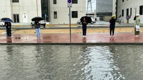 Des habitants de Dubaï attendent à côté d'une rue inondée, le 12 février 2024