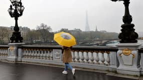 Une femme avec un parapluie marche sur le pont Alexandre III par une journée brumeuse le 30 mars 2022, à Paris.