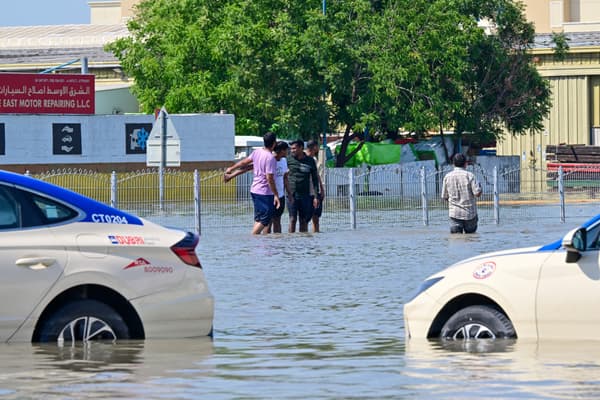Des personnes se tiennent près de voitures bloquées dans une rue inondée de Dubaï à la suite de fortes pluies, le 18 avril 2024.