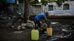 Un homme remplit des bidons d'eau près du bidonville "Talus 2" à Koungou, en cours de démolition, sur l'île française de Mayotte dans l'océan Indien, le 23 mai 2023