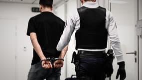 Un jeune homme avec des menottes suivi par un policier, le 5 avril 2019