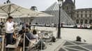 Un serveur sur une terrasse de restaurant près de la Pyramide du Louvre, conçue par l'architecte sino-américain Ieoh Ming Pei, au musée du Louvre, l'un des lieux qui sera rafraîchi avec l'eau de la Seine