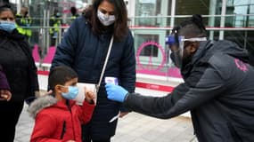 Un employé (d) prend la température de visiteurs voulant monter à bord du London Eye, attraction touristique en bord de Tamise, à Londres, le 17 mai 2021