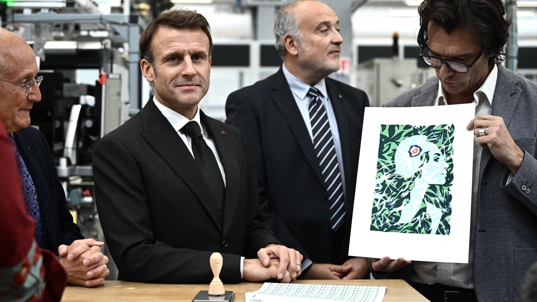 Le président français Emmanuel Macron, flanqué du PDG du groupe "La Poste" Philippe Wahl (à gauche) et du président de Philaposte Paul Dworkin (au centre), est présenté par l'illustrateur français Olivier Balez (à droite) le nouveau visage de Marianne qui sera représenté sur les timbres français de La Poste à l'imprimerie nationale de timbres Philaposte lors d'une cérémonie de dévoilement à Boulazac, dans le sud-ouest de la France, le 7 novembre 2023. 