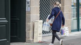 Une femme rentre chez elle avec des bouteilles d'eau et du papier hygiénique, à Nantes, le 17 mars 2020, alors qu'un strict confinement est entré en vigueur pour stopper la propagation du Covid-19.