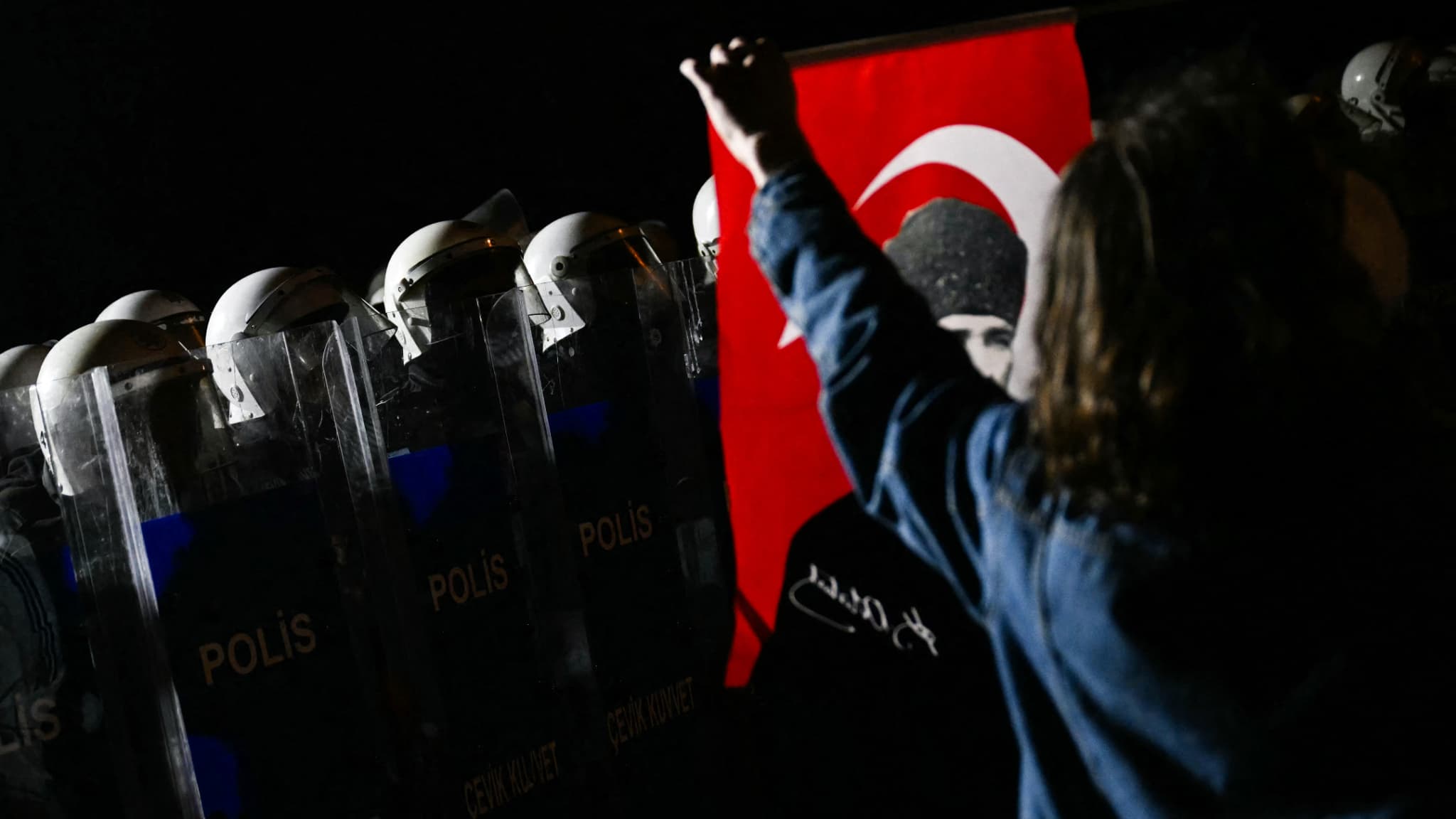 Un manifestant tient un drapeau turc avec une photo du père fondateur de l'État moderne turc, Mustafa Kemal Ataturk, devant des policiers anti-émeutes turcs lors d'un rassemblement de soutien au maire d'Istanbul arrêté, près de l'hôtel de ville d'Istanbul (Turquie), le 24 mars 2025. 
