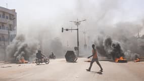 Un homme traverse des barricades en feu dans les avenues centrales de Ouagadougou le 23 janvier 2022. Des soldats se sont mutinés dimanche dans plusieurs casernes du Burkina Faso pour exiger le départ des chefs d'armée et des "moyens plus adaptés" pour lutter contre les jihadistes qui frappent ce pays depuis 2015.