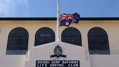 Le drapeau australien flotte en berne au Bondi Surf Bathers Life Saving Club, près de la promenade de Bondi Beach, où des personnes en deuil ont déposé des fleurs en hommage aux victimes de la fusillade qui s'est produite à cet endroit le 14 décembre, à Sydney, le 18 décembre 2025.